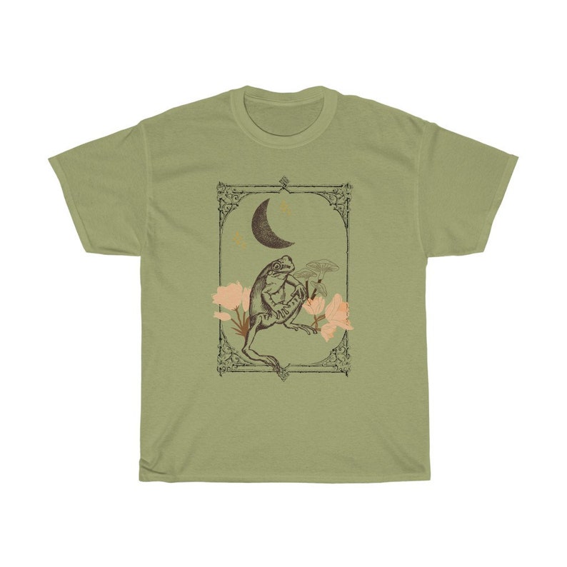 K&ouml;nnte beinhalten: Ein gr&uuml;nes T-Shirt mit einer Vintage-Illustration einer sitzenden Kr&ouml;te unter einem Halbmond mit Sternen und Blumen. Die Illustration ist mit einem dekorativen Rahmen versehen.
