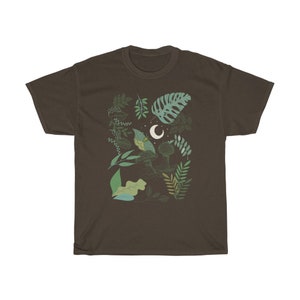 May include: A dark brown t-shirt with a green and white illustration of leaves, a crescent moon, and a bird. The illustration is centered on the shirt.