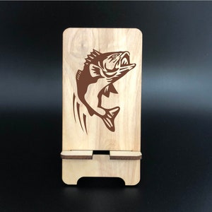 May include: A wooden phone stand with a brown graphic of a leaping fish. The stand is made of light-colored wood and has a slot to hold a phone. The fish graphic is detailed and stylized.