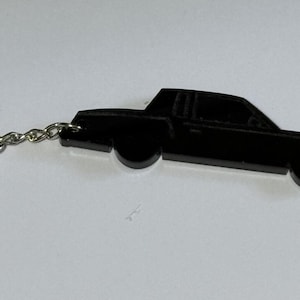 May include: A black car keychain with a silver key ring. The car is a silhouette of a classic car.
