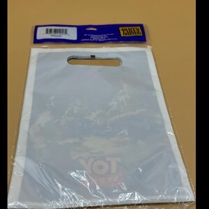 May include: A clear plastic shopping bag with a die-cut handle, sealed at the bottom. The bag has a white border and a printed design visible through the plastic. The top of the bag has a blue and yellow label.