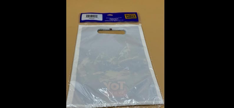 May include: A clear plastic shopping bag with a die-cut handle, sealed at the bottom. The bag has a white border and a printed design visible through the plastic. The top of the bag has a blue and yellow label.