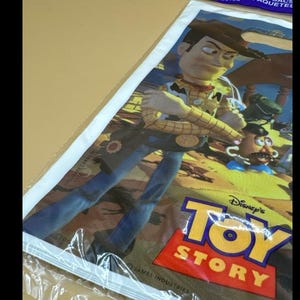 May include: A poster featuring Woody from Disney's Toy Story. Woody is depicted in a cowboy outfit, with a yellow shirt, brown vest, and blue jeans. The poster has the Toy Story logo in red and yellow.