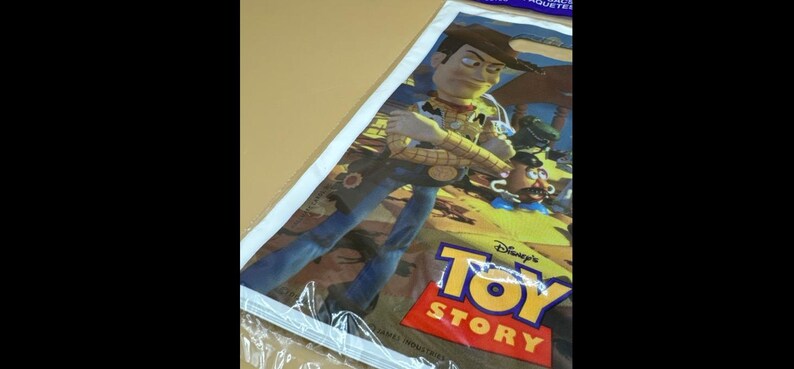 May include: A poster featuring Woody from Disney's Toy Story. Woody is depicted in a cowboy outfit, with a yellow shirt, brown vest, and blue jeans. The poster has the Toy Story logo in red and yellow.