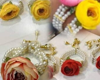 Op de afbeelding: Bloemenpols corsages met parelarmbanden en gouden accenten. De corsages hebben gele, roze en rode stoffen bloemen. De armbanden zijn gemaakt van witte parels en goudkleurig metaal.