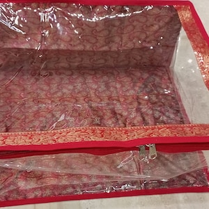 May include: Red fabric storage bag with a clear plastic window and gold trim. The bag has a zipper closure.