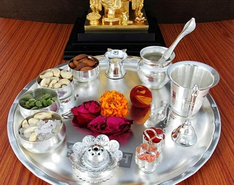 May include: A silver tray with a variety of items for a religious ceremony. The tray includes a small silver pitcher, a silver bowl, a silver spoon, a silver bell, a silver incense burner, and a small silver dish with red and pink decorations. There are also several small bowls filled with nuts, seeds, and sugar.