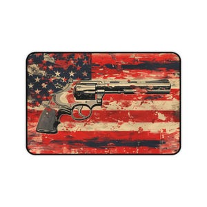 May include: A rectangular mousepad featuring a revolver superimposed over a distressed American flag design. The flag's red and white stripes are visible, with the blue field and stars in the upper left corner. The revolver is detailed with metallic and black accents.