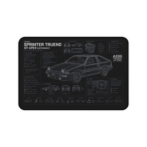May include: A black rectangular desk mat featuring a white technical line drawing of a Toyota Sprinter Trueno GT-Apex hatchback. The design includes detailed specifications, engine diagrams, and dimensions in imperial units, with text labels.