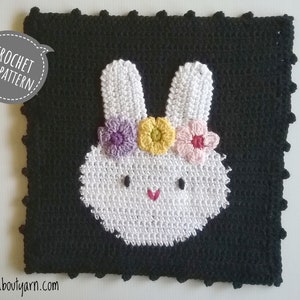Puede incluir: Patrón de crochet para un conejito blanco con una corona de flores. El conejito está sobre un fondo negro con el texto "CROCHET PDF PATTERN" en un bocadillo.