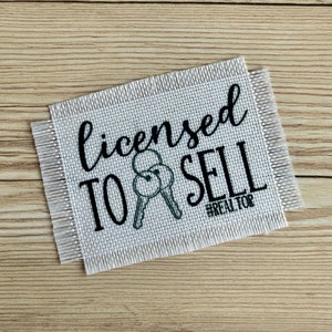 May include: White canvas patch with black text that reads "licensed to sell #REALTOR" with a black and gray illustration of two keys.