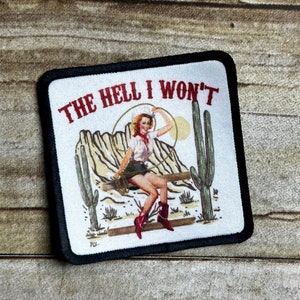 May include: A white patch with black edging features a cartoon image of a woman in a cowboy hat and outfit sitting on a log in a desert landscape. The text "THE HELL I WON'T" is printed in red above the image.