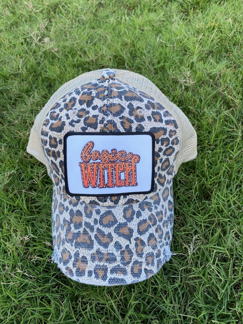 May include: A leopard print trucker hat with a patch that says "basic witch" in orange letters.