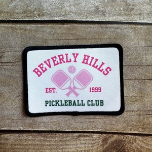 May include: White patch with black border, featuring the text "Beverly Hills Pickleball Club" in pink and green lettering. The patch also includes a pink pickleball paddle and ball graphic with the text "Est. 1999".