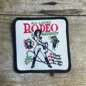 May include: A white square patch with black edging. The patch features a vintage-style illustration of a woman in a cowboy hat and boots, holding a lasso. The text "ALL-LADIES RODEO & ROUNDUP" is in red and green lettering. The text "SAT JULY 4TH" is in black lettering. The text "*Ropin' *Wrasslin' *No Critter Too Big!" is in green lettering.