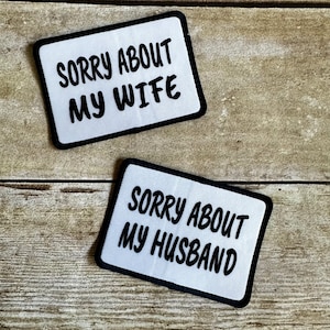 May include: Two white patches with black borders and text. The top patch says "SORRY ABOUT MY WIFE". The bottom patch says "SORRY ABOUT MY HUSBAND".