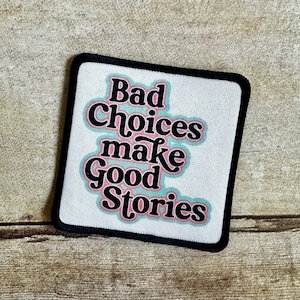 May include: White square patch with black border and the text "Bad Choices Make Good Stories" in black with a pink and blue outline.