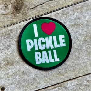May include: A round patch with a green background and the words "I PICKLE BALL" in white. A pink heart is above the word "PICKLE". The patch has a black border.