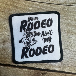 May include: White patch with black text and a black and white image of a person riding a horse. The text reads "Your Rodeo Ain't My Rodeo".