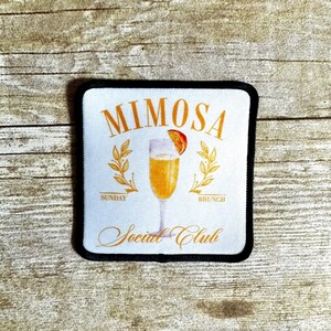 May include: White patch with black trim featuring a gold illustration of a mimosa with an orange slice. The text "Mimosa Social Club" is written in gold script with the words "Sunday" and "Brunch" written in gold below the illustration.