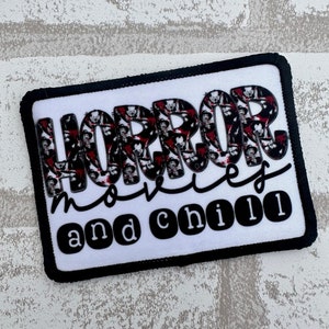 May include: White iron-on patch with black trim. The patch features a graphic of horror movie characters in the word "HORROR" with the text "movies and chill" below.