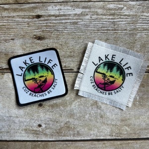 May include: Two square patches with the words "Lake Life" and "Cuz Beaches Be Salty". One patch is white with a black border, the other is a woven white patch. The patches feature a colorful graphic of a lake scene.