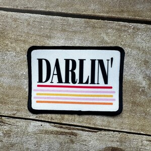 May include: White patch with black text that reads "DARLIN'" with five colorful stripes underneath.