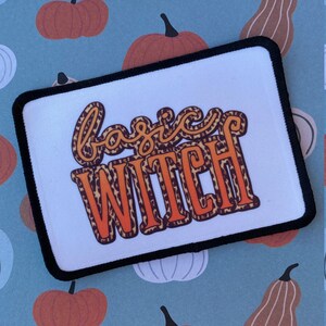 May include: A white patch with black edging features the text "basic witch" in orange and brown leopard print lettering.