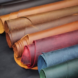 Puede incluir: Múltiples rollos de cuero en varios colores, incluyendo tonos marrón, bronceado, rojo intenso, azul y verde. Cada rollo muestra una textura de superficie lisa y mate con grano natural visible y bordes que muestran la parte inferior fibrosa.