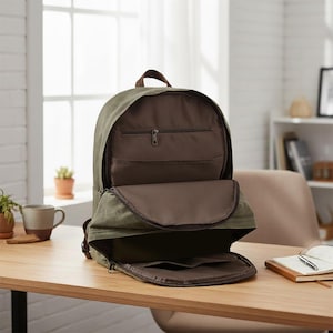 May include: An open olive green canvas backpack with brown interior pockets and a brown handle. The backpack is sitting on a wooden table, showcasing its interior compartments and design.