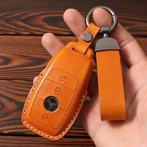 May include: A brown leather key fob with a metal ring and a strap. The fob has a stitched design and a clear plastic window.