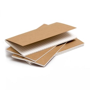 Puede incluir: Una pila de pequeños cuadernos de papel kraft marrón con páginas blancas rayadas. Los cuadernos están abiertos, revelando las páginas interiores, y están dispuestos en un patrón ligeramente superpuesto sobre un fondo blanco.