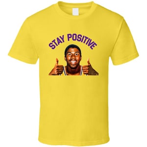 May include: Yellow t-shirt with a purple "STAY POSITIVE" text and a photo of a smiling basketball player giving a thumbs up with both hands.