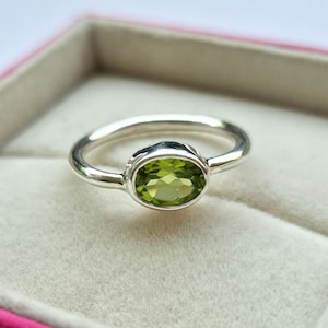 May include: A silver ring with a green oval gemstone. The ring is in a white box.