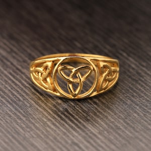 May include: A gold ring with a Celtic knot design. The knot is in the shape of a triangle and is surrounded by a circle.
