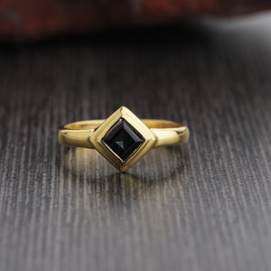 May include: A gold ring with a square-shaped black gemstone set in a diamond-shaped frame.