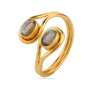 Pu&ograve; includere: Un anello dorato con due pietre preziose ovali grigio-blu. L'anello presenta un design continuo ad anello, con le pietre incastonate in castoni individuali. L'anello &egrave; presentato su sfondo bianco.