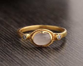 Puede incluir: Un anillo de oro con una gran piedra preciosa ovalada transparente y dos piedras preciosas transparentes más pequeñas a cada lado.
