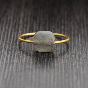 Può includere: Un anello d'oro con una pietra preziosa di labradorite di forma quadrata, di colore grigio.