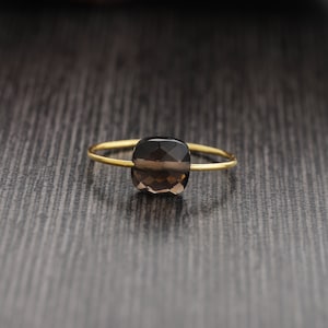 May include: A gold ring with a dark brown, faceted gemstone. The ring is on a dark wood surface.