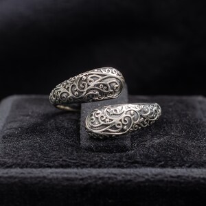 Op de afbeelding: Een zilveren ring met een zwierig, ingewikkeld ontwerp. De ring is open en lijkt verstelbaar te zijn.