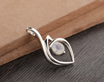 May include: A silver pendant with a leaf-like design, featuring a small, round, iridescent gemstone. The pendant is set against a brown and black background, highlighting its polished metal and the subtle colors of the stone.