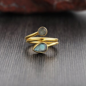 Puede incluir: Anillo de oro con dos piedras preciosas de labradorita en forma de lágrima. El anillo está envuelto dos veces alrededor del dedo.