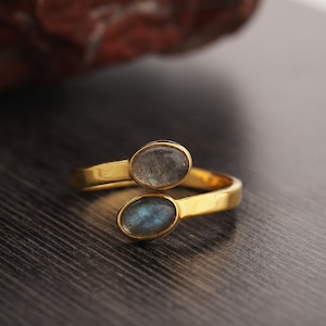 May include: A gold ring with two oval-shaped labradorite gemstones. The ring is designed to wrap around the finger.