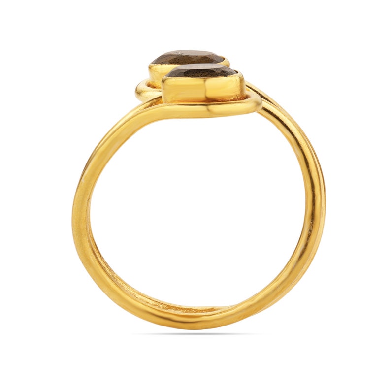Pu&ograve; includere: Un anello dorato con due pietre preziose scure di forma ovale. La fascia dell'anello si curva con grazia, con le pietre preziose poste una accanto all'altra nella parte superiore. Il design &egrave; semplice ma elegante, con un'estetica minimalista.