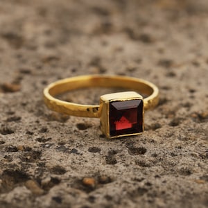 May include: A gold ring with a square, dark red gemstone.