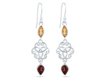 Puede incluir: Un par de pendientes colgantes de plata. Cada pendiente presenta una gema de color ámbar, con corte marquesa, una filigrana decorativa de plata y una gema roja oscura en forma de lágrima. Los pendientes cuelgan de un simple gancho de plata.