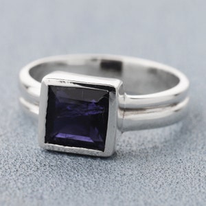 Peut inclure: Une bague en argent avec une pierre précieuse carrée de couleur violet foncé sertie dans un sertissage à bélière. La bague a une double bande.