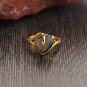 Può includere: Un anello d'oro con una pietra preziosa grigio scuro incastonata in un design a forma di cuore.