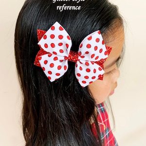 Pu&ograve; includere: Un fiocco bianco con pois rossi e dettagli glitter. Il fiocco &egrave; legato con un nastro rosso e viene indossato nei capelli di una bambina.